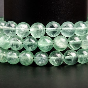 May include: A strand of light green gemstone beads, likely fluorite, arranged in a circular pattern. The beads are smooth and translucent, with a slight shimmer.