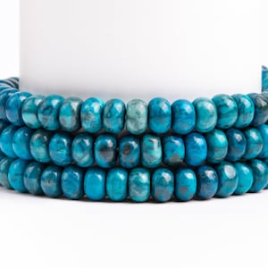 May include: A strand of turquoise blue gemstone beads, with a smooth, polished finish. The beads are round and have a slightly irregular shape. The beads are stacked on top of each other, creating a layered effect.