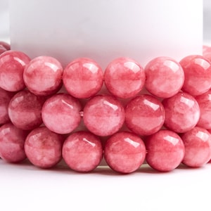 May include: A close-up of a stack of pink gemstone beads. The beads are round and smooth, and they have a slightly translucent appearance.