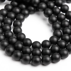 May include: A strand of black matte round beads. The beads are strung together to form a necklace or bracelet.