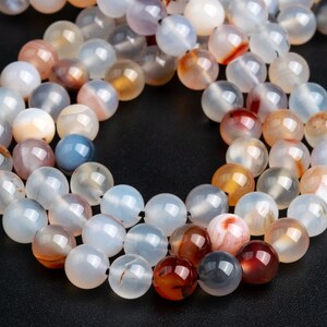 May include: A strand of round, translucent agate beads with brown, red, and white patterns. The beads are strung together on a thin, black thread.
