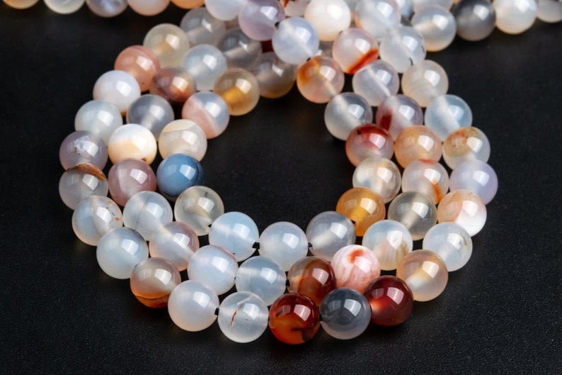 May include: A strand of round, translucent agate beads with brown, red, and white patterns. The beads are strung together on a thin, black thread.