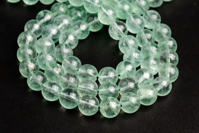May include: A strand of light green gemstone beads. The beads are round and smooth, and they have a translucent appearance.