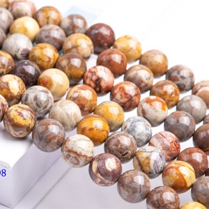 May include: A strand of brown, yellow, and white agate beads. The beads are round and have a polished finish. The beads are strung on a clear string.