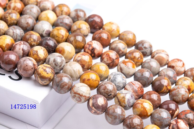 May include: A strand of brown, yellow, and white agate beads. The beads are round and have a polished finish. The beads are strung on a clear string.