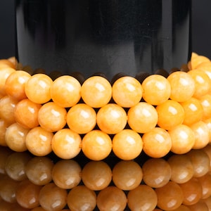 May include: A close-up of a bracelet made of multiple strands of round, orange-colored beads. The beads are smooth and polished, and they are arranged in a symmetrical pattern.