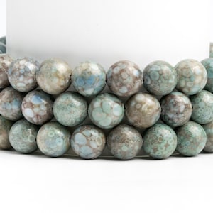 May include: A strand of round, blue and grey speckled beads. The beads are made of glass and have a mottled, marbled appearance.