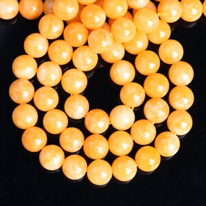 May include: A strand of round, orange gemstone beads. The beads are smooth and have a slight shimmer.