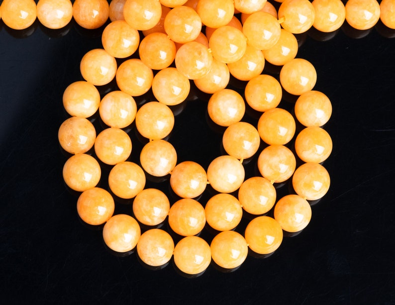 May include: A strand of round, orange gemstone beads. The beads are smooth and have a slight shimmer.