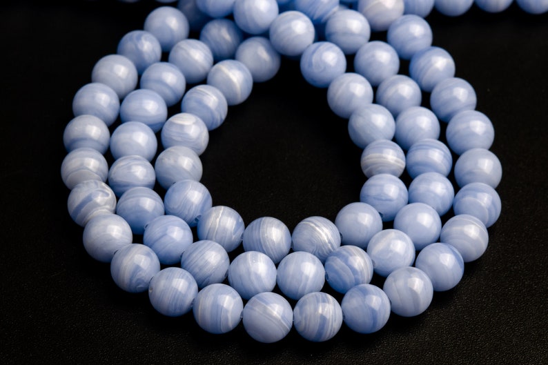 May include: A strand of light blue agate beads with white swirls. The beads are round and smooth, and they are arranged in a circular pattern.