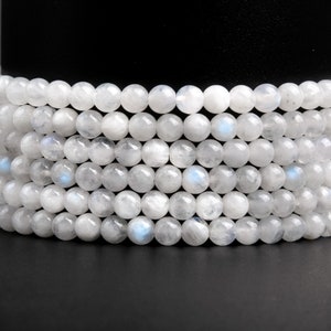 May include: A strand of white moonstone beads, stacked and arranged in a circular pattern. The beads are round and smooth, with a subtle iridescent sheen.