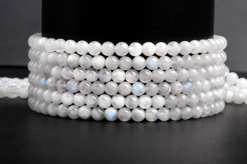 May include: A strand of white moonstone beads, stacked and arranged in a circular pattern. The beads are round and smooth, with a subtle iridescent sheen.