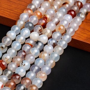 May include: A strand of white agate beads with brown and red inclusions. The beads are round and smooth, and they are strung on a clear thread.