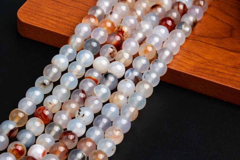 May include: A strand of white agate beads with brown and red inclusions. The beads are round and smooth, and they are strung on a clear thread.
