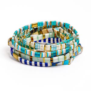 May include: A stack of multi-strand bracelets composed of rectangular beads in shades of turquoise, navy blue, white, and translucent pale green, interspersed with small metallic gold spacers. The beads are arranged in repeating color patterns.