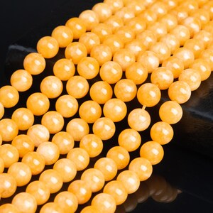 May include: A strand of yellow gemstone beads. The beads are round and smooth, and they have a slightly translucent appearance. The beads are strung on a clear thread.