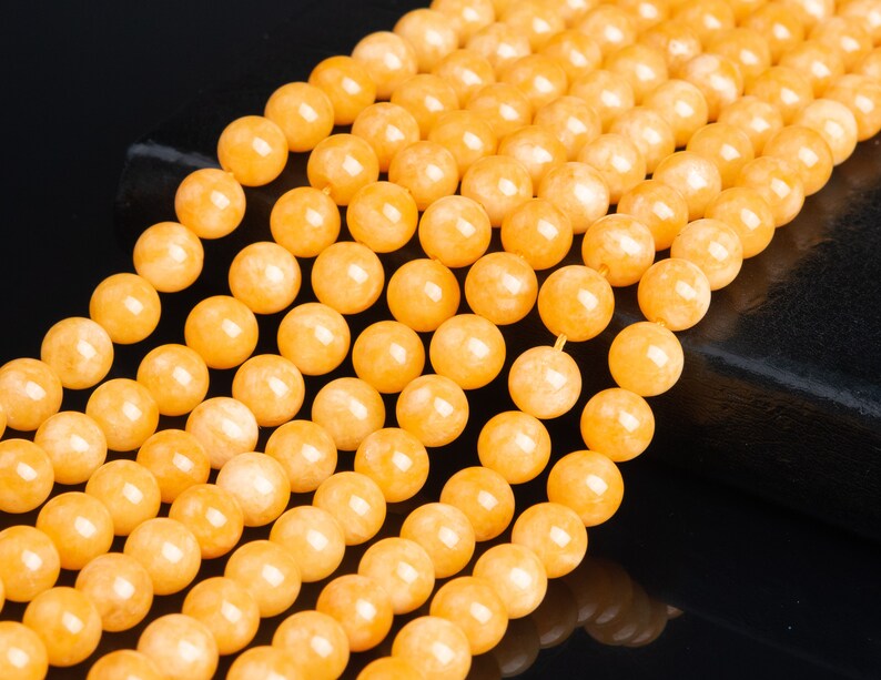 May include: A strand of yellow gemstone beads. The beads are round and smooth, and they have a slightly translucent appearance. The beads are strung on a clear thread.