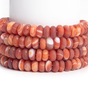 May include: A close-up of a strand of carnelian beads. The beads are a deep orange color with white stripes. The beads are stacked on top of each other, creating a layered effect.