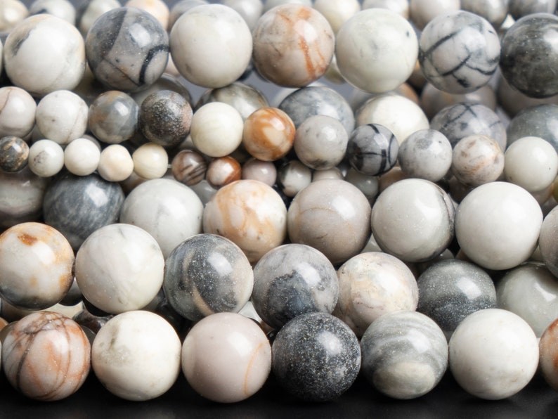 May include: A collection of round, smooth, white, gray, and brown agate beads with natural patterns. The beads are approximately 1 inch in diameter.