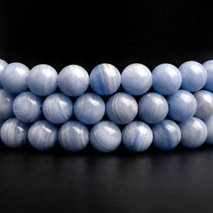 May include: A strand of blue agate beads, with a smooth, polished finish. The beads are round and have a light blue color with white streaks.
