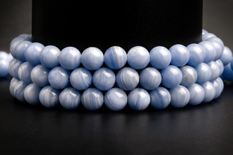 May include: A strand of blue agate beads, with a smooth, polished finish. The beads are round and have a light blue color with white streaks.