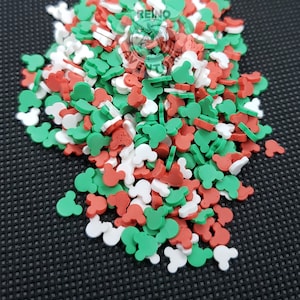 May include: A pile of colorful Mickey Mouse-shaped sprinkles in red, white, and green. These decorative sprinkles are perfect for adding a festive touch to baked goods, desserts, and other treats. The sprinkles are scattered on a dark surface.