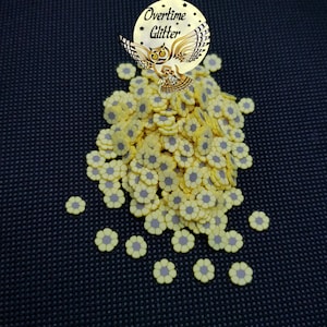 May include: A large pile of yellow flower-shaped sprinkles with gray centers. The sprinkles are scattered on a black surface.