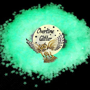 May include: A pile of light green star-shaped glitter on a black background. The glitter surrounds a circular logo with an owl illustration and the words "Overtime Glitter". The owl is brown and gold.
