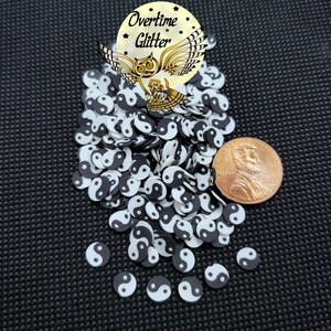 May include: A pile of black and white yin yang symbol sprinkles with a penny for scale. The sprinkles are small and round, and they are perfect for decorating cakes, cupcakes, and other desserts.