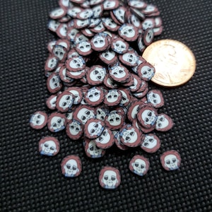May include: A collection of small, round polymer clay slices featuring a cartoon character face with a white mask, brown hair, and a blue shirt. The slices are scattered on a dark surface, with a penny for size comparison.