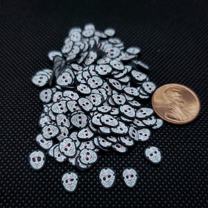 May include: A large pile of white and black hockey mask shaped sprinkles with red accents. The sprinkles are about the size of a US penny.