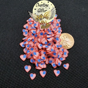May include: A pile of heart-shaped polymer clay pieces in red, white, and blue, resembling the American flag. A penny is next to the clay hearts. The image also includes a gold sticker with an owl and the words "Overtime Glitter".