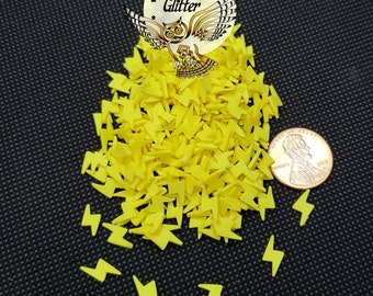 May include: A pile of yellow lightning bolt shaped sprinkles, next to a US penny for scale. The sprinkles are for decorating cakes, cupcakes, and other baked goods.