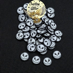 May include: A pile of white and black Jack Skellington face-shaped embellishments. The embellishments have a black border and a smiling face design. The image also includes a gold sticker with the text "Overtime Glitter" and an owl graphic.