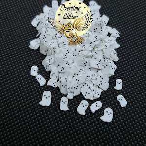 May include: White ghost sprinkles with black eyes. The sprinkles are in a pile on a black background. The text "Overtime Glitter" is visible in the image.