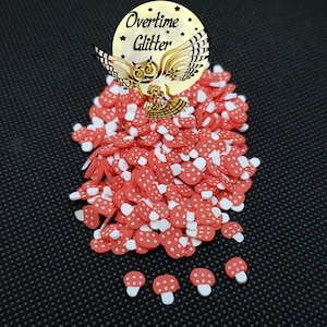 May include: A large pile of red and white mushroom-shaped sprinkles. The sprinkles are scattered on a black surface. There are also a few smaller sprinkles in the bottom right corner of the image.