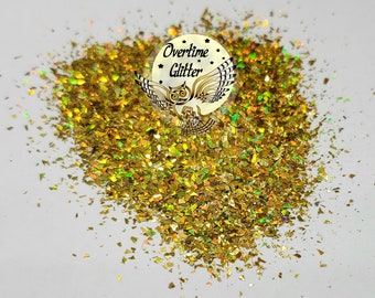Pode incluir: Um monte de flocos de glitter iridescentes de cor dourada com um logótipo circular apresentando uma coruja e o texto Overtime Glitter. As peças pequenas, reflexivas e de aspeto metálico estão espalhadas de forma irregular.