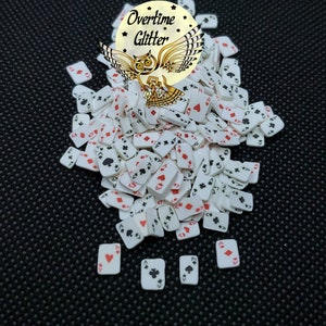 May include: A pile of white playing card shaped confetti with red and black suits. The confetti is on a black background with a small white owl logo that says "Overtime Glitter".