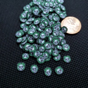 May include: A pile of small, round polymer clay beads featuring a cartoon character face with green hair, white skin, and a black and white suit. The beads are primarily green, white, and black. A U.S. penny is included for size reference.