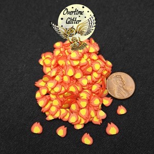 May include: A pile of small, red and yellow flame-shaped sprinkles, with a penny for scale. The sprinkles are perfect for adding a touch of fire to your crafts.