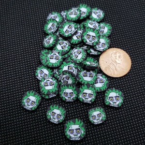 May include: A pile of green and black round stickers with a cartoon zombie face on each one. The stickers are about the size of a US penny.