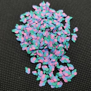 May include: A large pile of small, colorful flower and leaf shaped sprinkles. The sprinkles are in shades of pink, blue, and green.