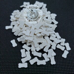 May include: A large pile of white plastic bone-shaped sprinkles. The sprinkles are scattered on a black surface. The image includes a logo that says "Reino Aventura".
