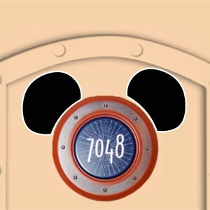 May include: A tan background with two large black circles and a circular emblem. The emblem has a silver rim, a red outer ring, and a blue inner design with the number 7048 in white.