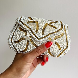 May include: A white beaded clutch purse with gold accents. The purse is decorated with a floral pattern.
