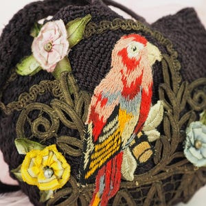 May include: A dark brown fabric purse with embroidered flowers and a parrot. The parrot is embroidered in shades of red, yellow, and blue.
