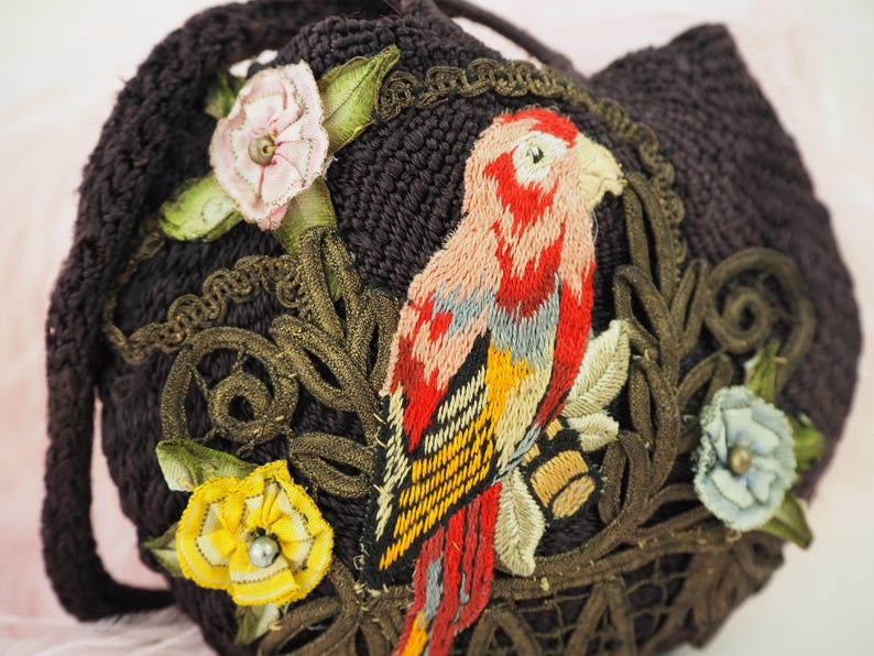 May include: A dark brown fabric purse with embroidered flowers and a parrot. The parrot is embroidered in shades of red, yellow, and blue.