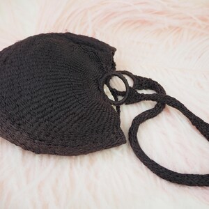 May include: A black crocheted tote bag with a single, thick strap. The bag is made of a woven material and has a round, open top.