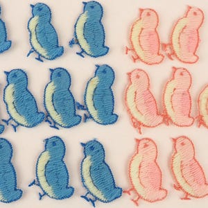 May include: Embroidered bird patches in blue and pink. The blue birds have a light yellow belly and the pink birds have a light yellow belly. The patches are arranged in rows on a white background. These patches are ideal for crafting and adding a decorative touch to clothing or accessories.