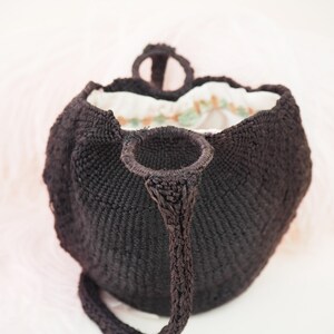 May include: A black woven tote bag with a single strap and a white and green floral lining.